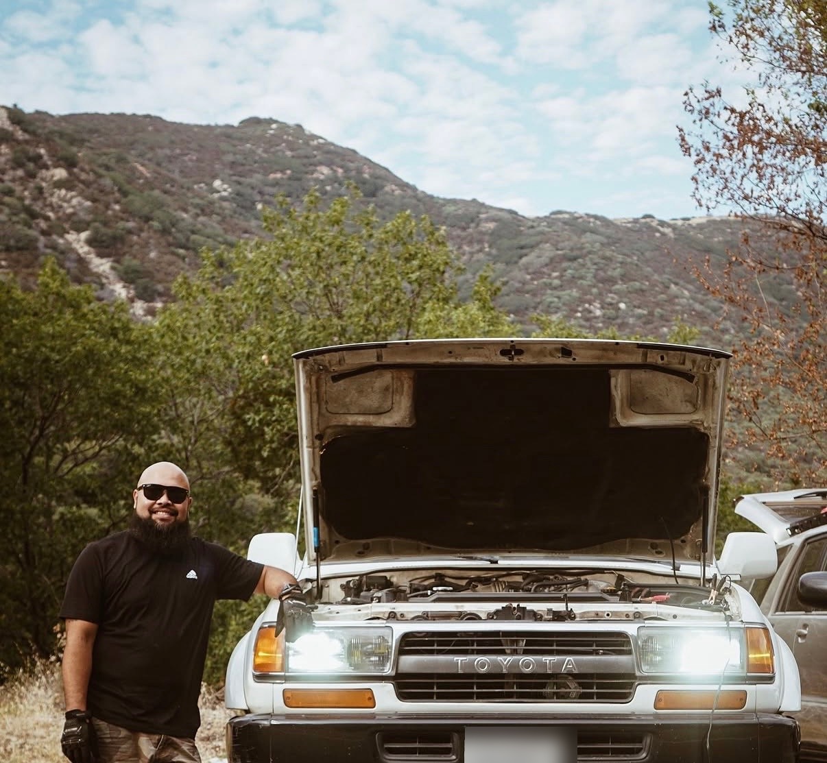 Jay standing beside the white Toyota Land Cruiser with its hood up on a mountain trail