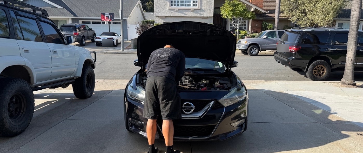 Jay working under the hood of a car in a suburban driveway